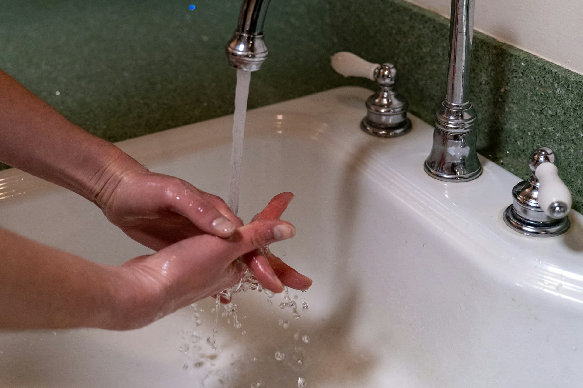 Person washing their hands under a running chrome tap at a white sink
